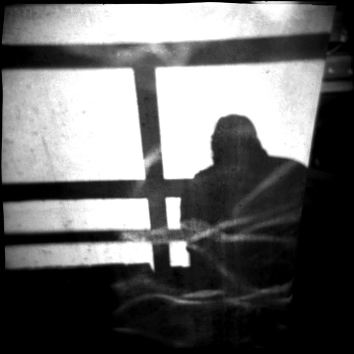 A silhouetted figure seen through a barred window in grainy black and white — present, but not fully legible.